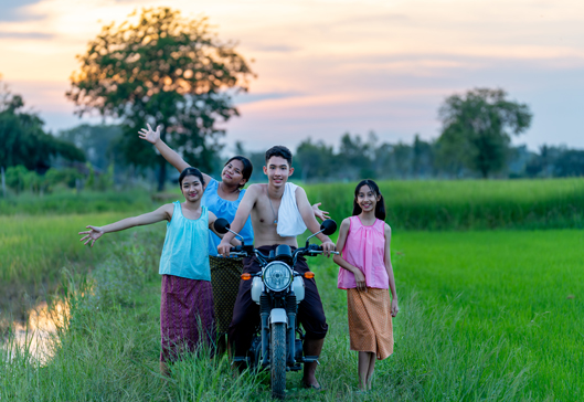 Asian boy sit on motorcycle and three girls stand near him and t