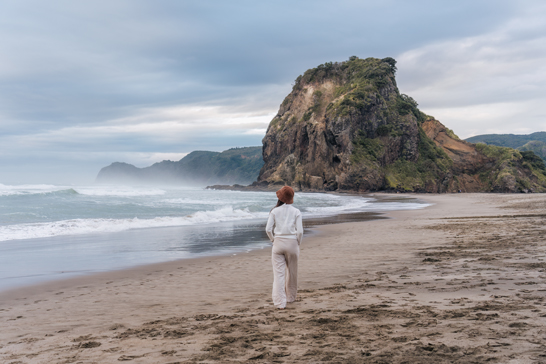 Happy young asian woman enjoying on the Piha Beach with Lion Rock at West of Auckland, New Zealand