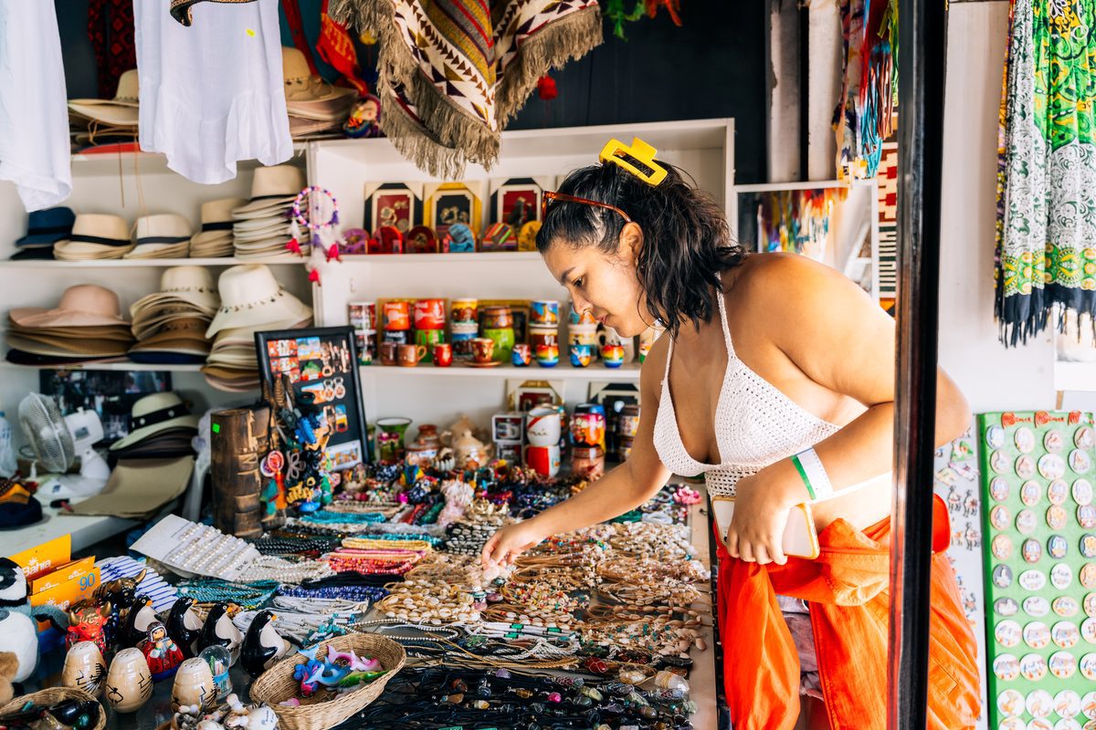 A woman browsing colourful handicrafts at a local Greek market stall — shopping local is one of the best budget travel tips for Greece