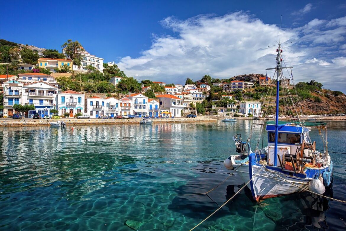 A traditional Greek fishing village harbour with crystal-clear turquoise water and colourful hillside houses — Greece off the beaten path