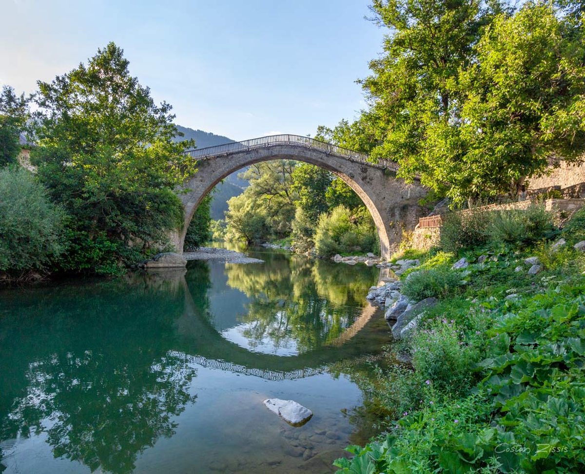 The ancient Vovousa stone bridge arching over a jade-green river in the Zagori region of Epirus — one of Greece's most spectacular hidden gems